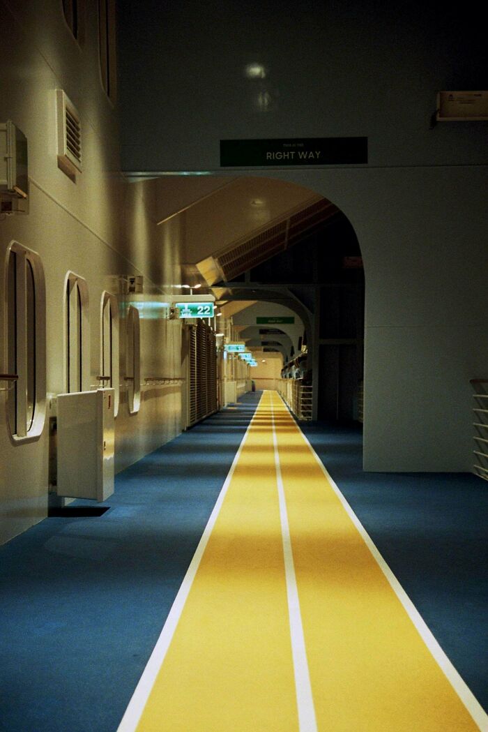 Dimly lit liminal space corridor with a yellow path and signs, evoking a creepy backrooms atmosphere.