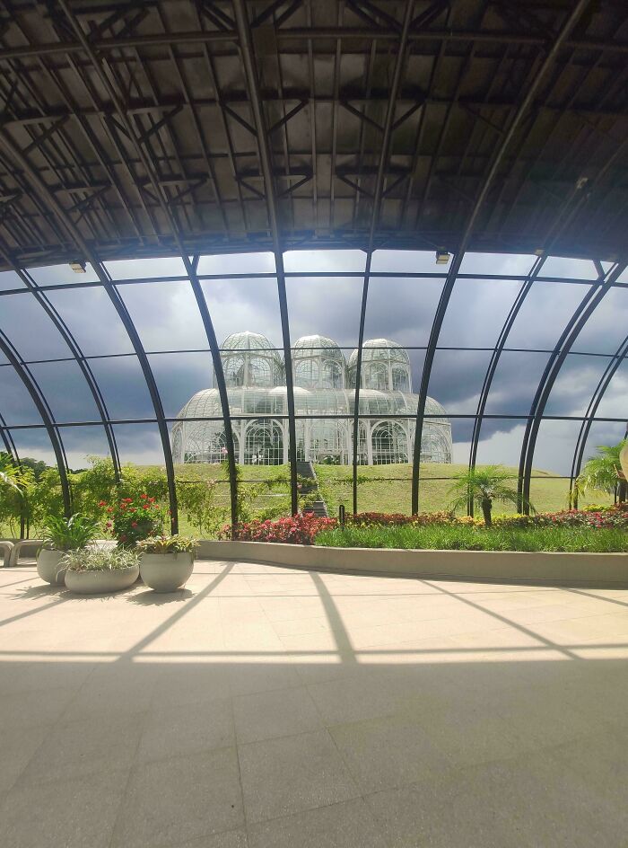 Curved glass structure with plants inside, view of dome-like greenhouse under dark cloudy sky in liminal spaces.