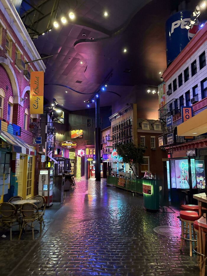 Indoor street with colorful neon lights and empty tables, creating a creepy liminal space resembling the backrooms.