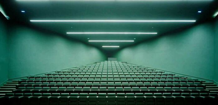 Empty lecture hall with green lighting and rows of seats, evoking creepy liminal spaces that resemble the Backrooms.