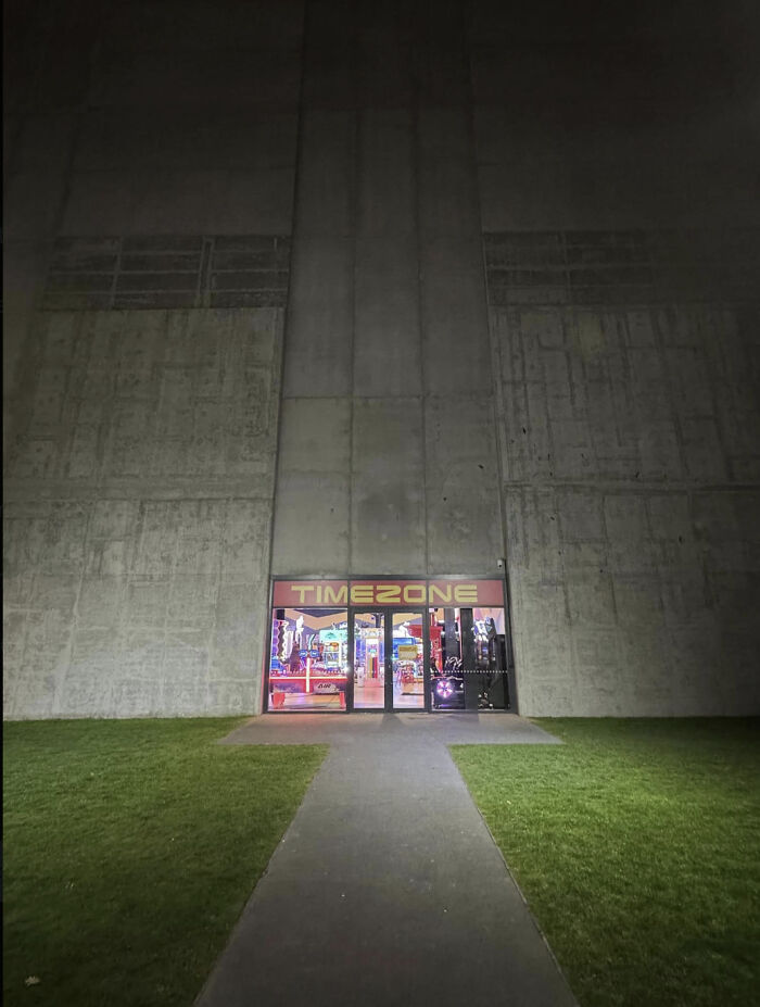 Dimly lit entrance to arcade with large concrete walls, evoking eerie liminal spaces similar to the Backrooms.