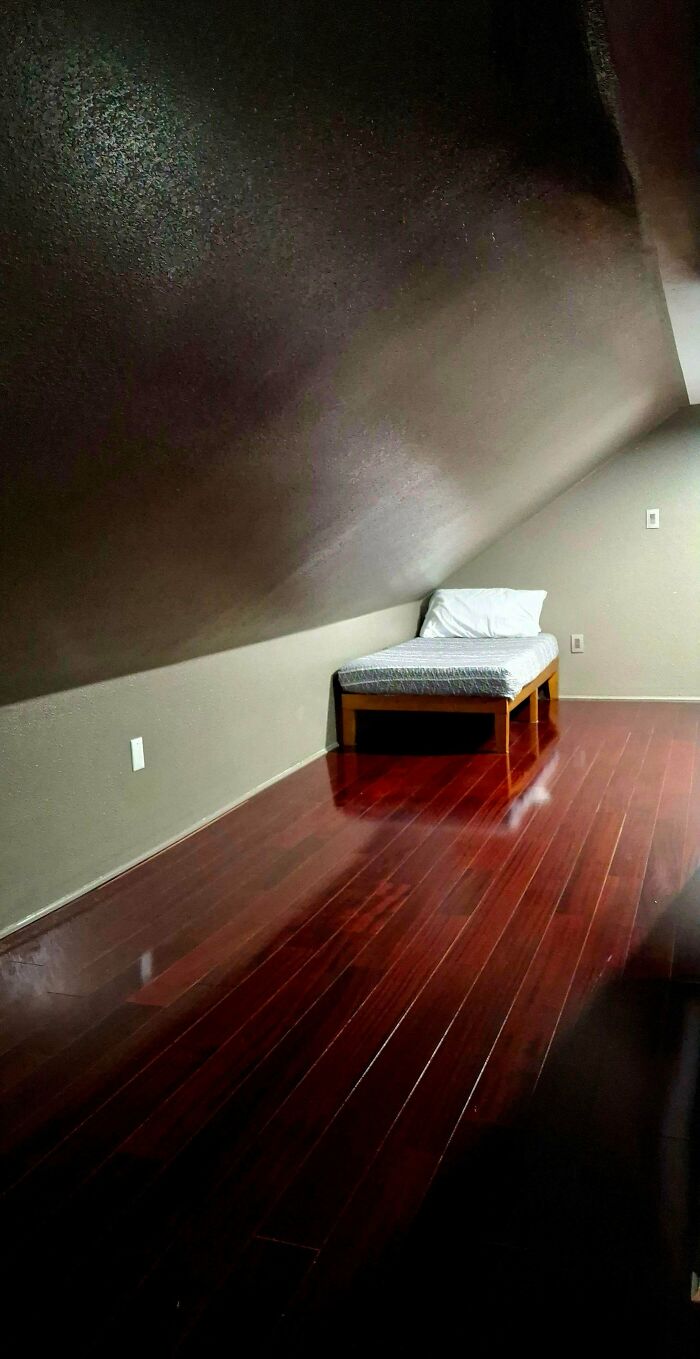 Small bed in a dim attic with slanted ceiling and dark wooden floors, evoking liminal spaces like the Backrooms.