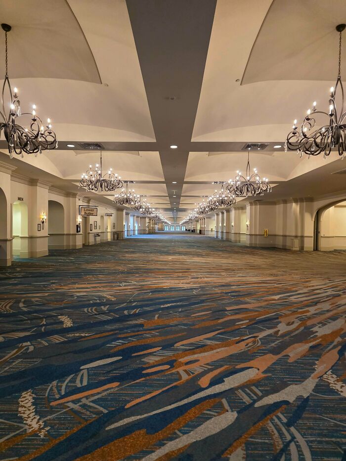 Empty liminal space corridor with chandeliers and patterned carpet, resembling creepy backrooms atmosphere.