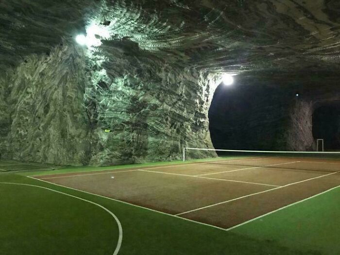 Indoor tennis court inside a cave-like liminal space with eerie lighting, resembling creepy backrooms atmosphere.