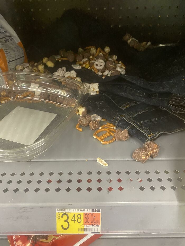Clear container and spilled snack mix with pretzels and chocolate pieces on a Walmart shelf, illustrating funny Walmart people.
