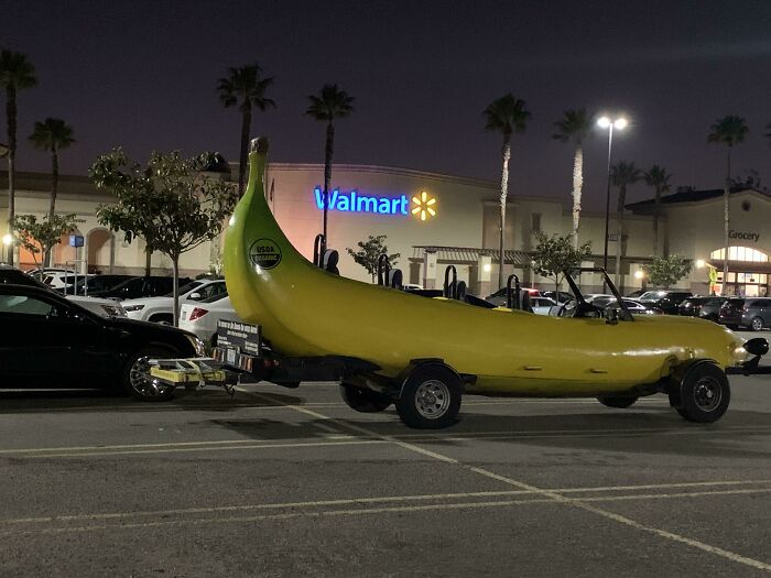 Large banana-shaped car parked in a Walmart parking lot at night with palm trees and other cars nearby.