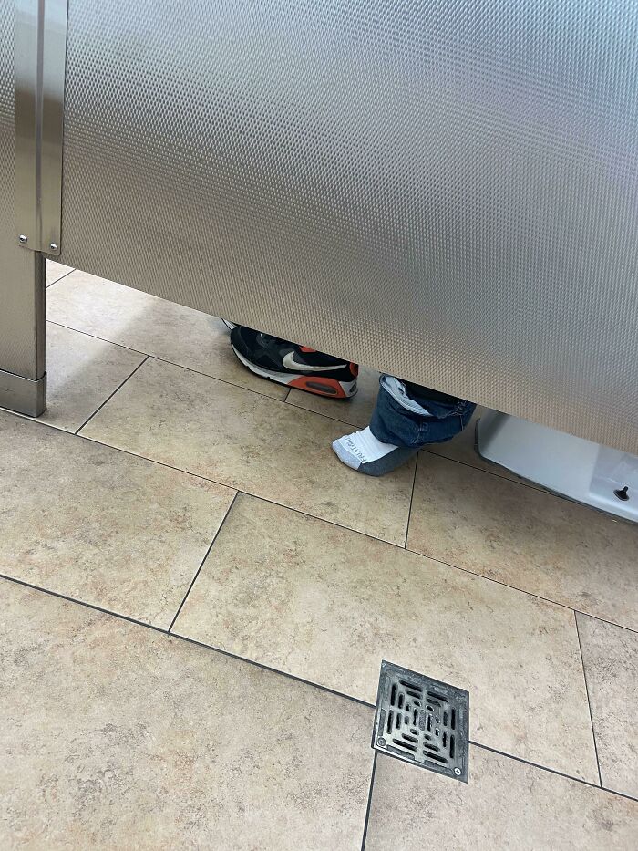 Shoes and one sock visible under a Walmart bathroom stall, showcasing a funny and confusing Walmart people moment.