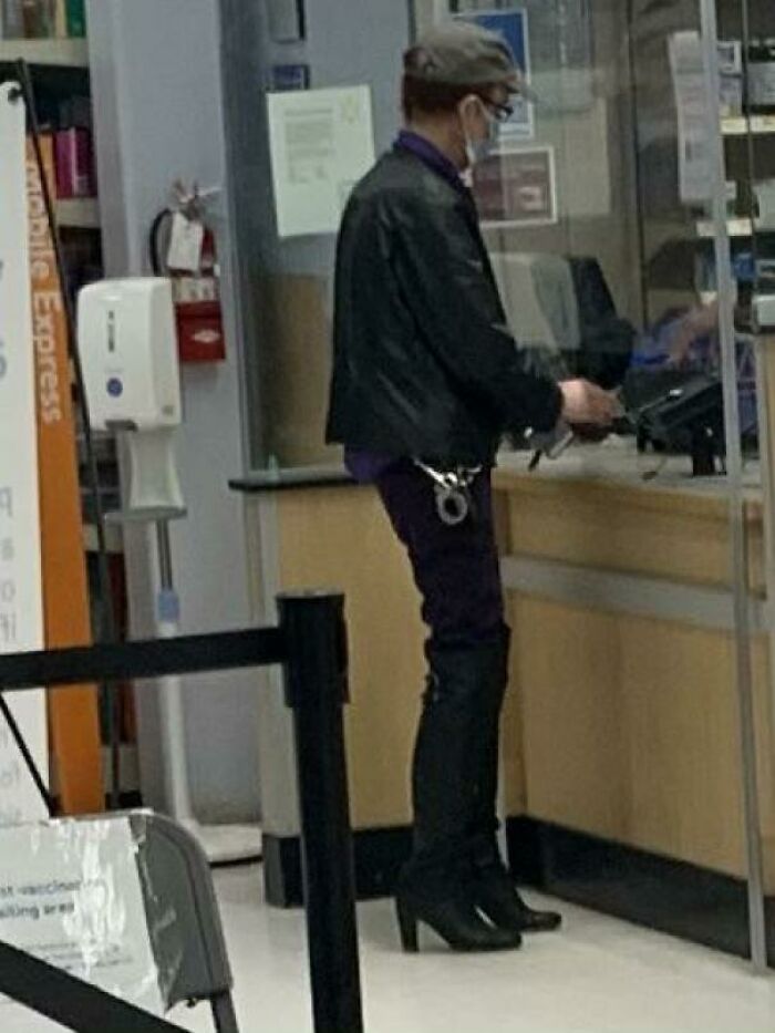 Man wearing high heel boots and handcuffs at a counter inside a store, a funny Walmart people moment.
