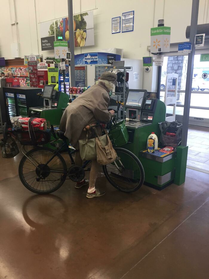 Elderly person with bicycle using self-checkout at Walmart with groceries and bags around them.