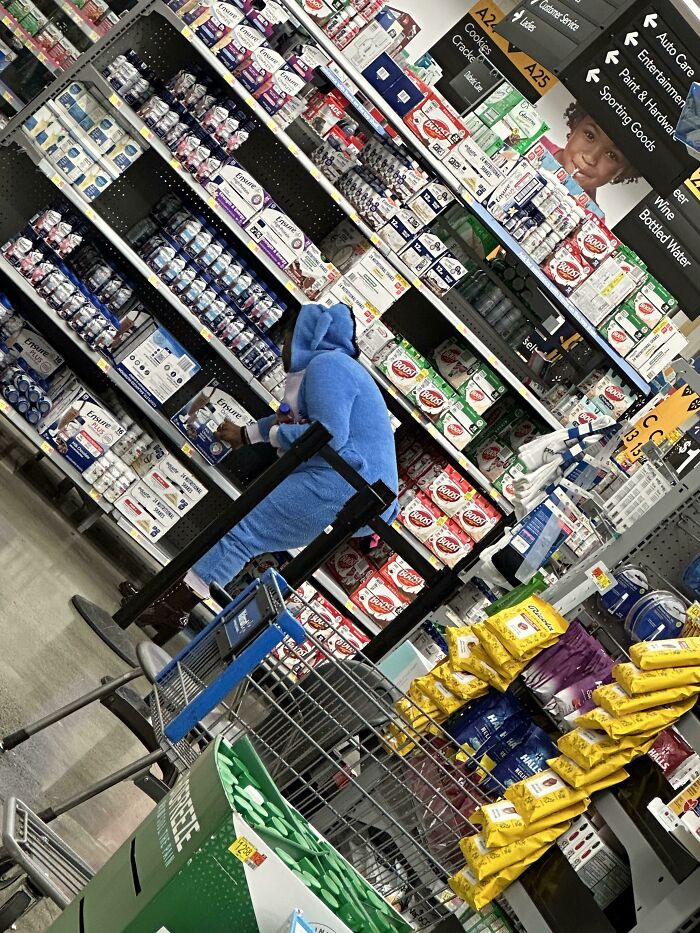 Person in a blue onesie shopping at Walmart aisle filled with health and nutrition products, creating a funny Walmart people moment.