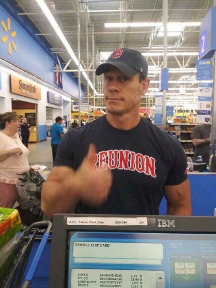 Man wearing reunion shirt giving thumbs up at Walmart checkout with store shelves and shoppers in the background.
