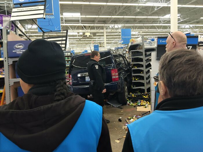 Black SUV crashed inside Walmart aisle with confused Walmart people and employees observing the chaotic store scene.