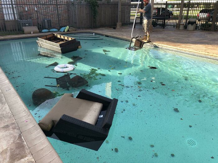 Patio furniture and cushions dumped in a swimming pool while worker skims debris, next-level jerks