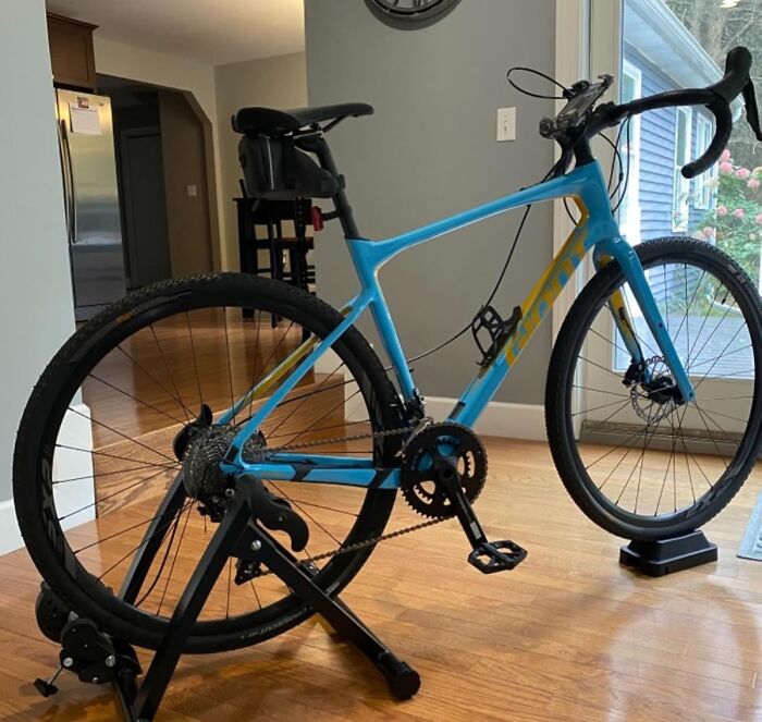 Blue road bike set on an indoor trainer in an apartment with hardwood floors, promoting apartment friendly fitness goals.
