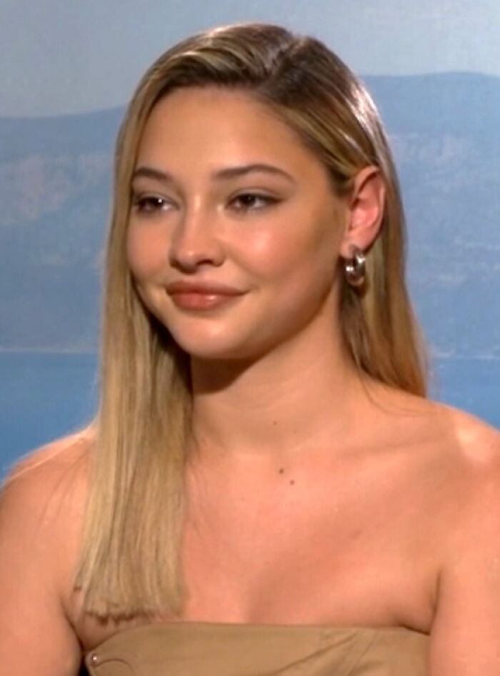 Madelyn Cline with long blonde hair and hoop earrings, smiling during an interview about her bio and career highlights.