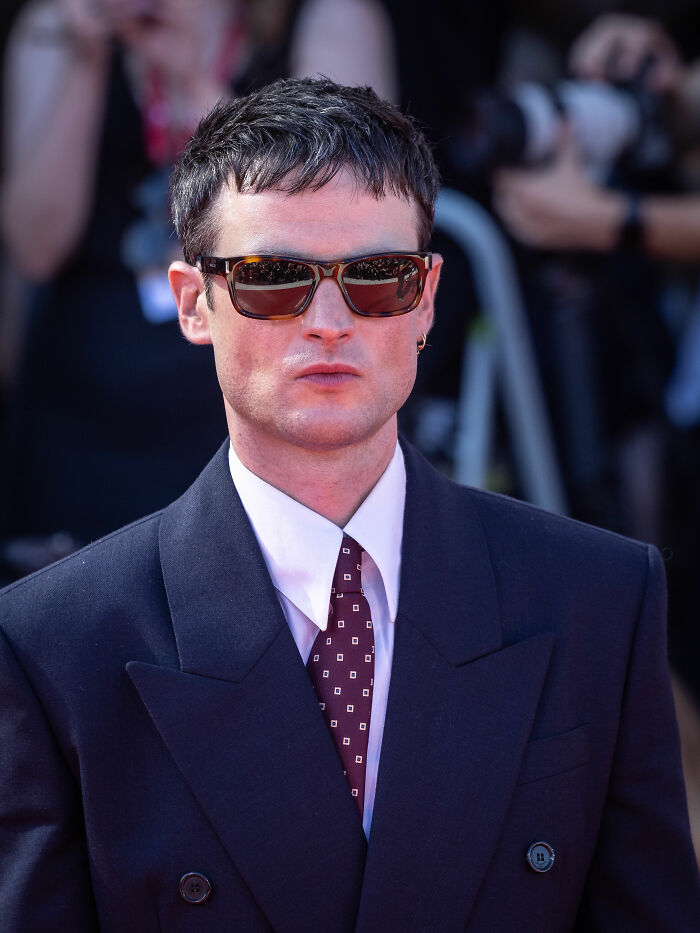 Tom Sturridge wearing sunglasses and a dark suit at a public event, highlighting his style and presence.