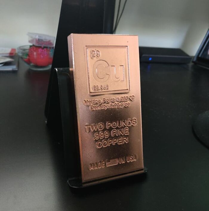 Copper bar with periodic table details and weight, one of the bizarre Christmas gifts people received, displayed on a desk stand.