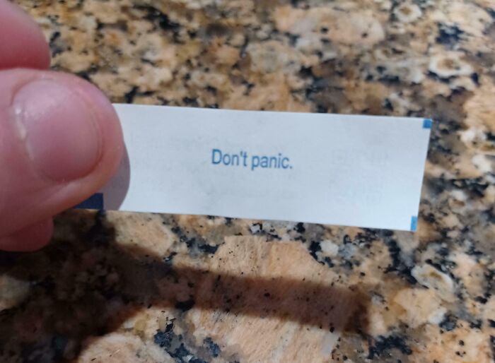 Funny pictures: close-up of hand holding a fortune slip that reads Don't panic on a speckled granite countertop