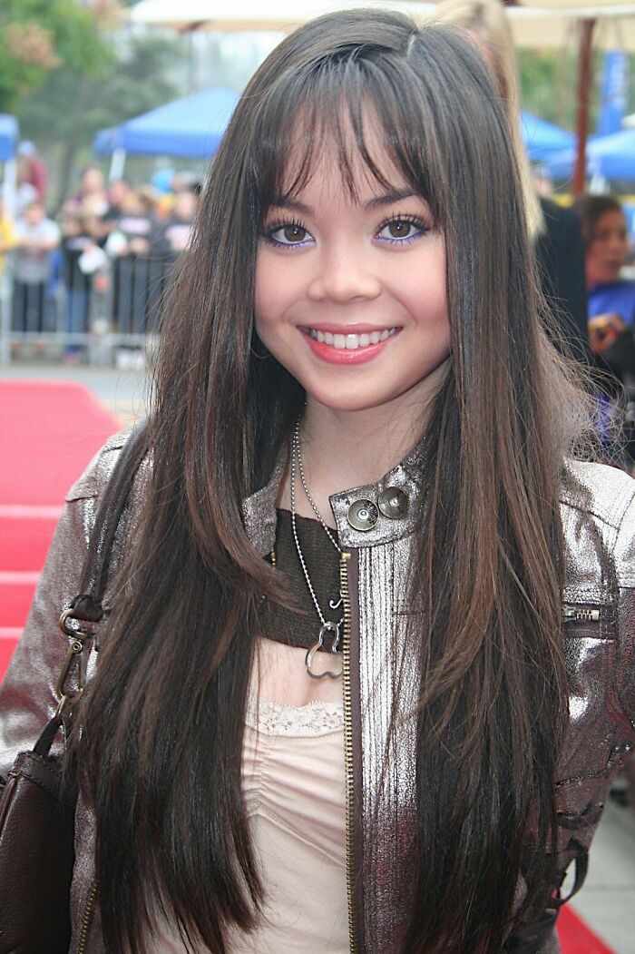 Anna Maria Perez de Tagle smiling on a red carpet, wearing a metallic jacket and long straight hair outdoors.