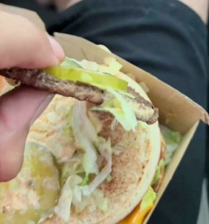 Close-up of a hamburger with pickles and lettuce, showing a thin beef patty in an interesting food moment.