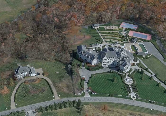 Aerial view of an impressive mansion with large green lawns, gardens, and tennis courts, showcasing interesting architecture.