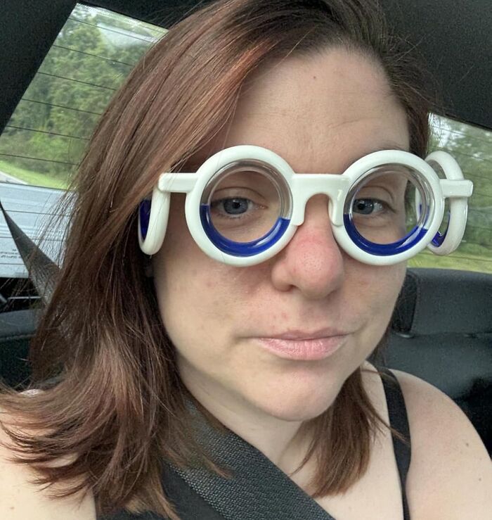 Woman wearing unusual round white and blue glasses inside a car, illustrating 25 best sellers and delusional trends in 2025.
