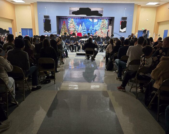 Crowded school auditorium holiday concert, center aisle view, next-level jerks theme