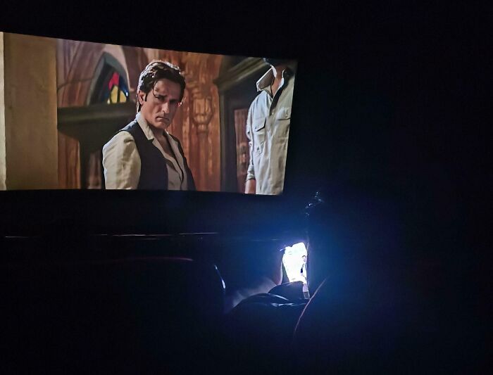 Movie theater patron using phone in dark, bright screen disturbing others — next-level jerks