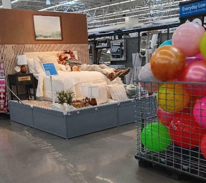 Person sprawled on store display bed beside bin of colorful balloons, an example of next-level jerks.