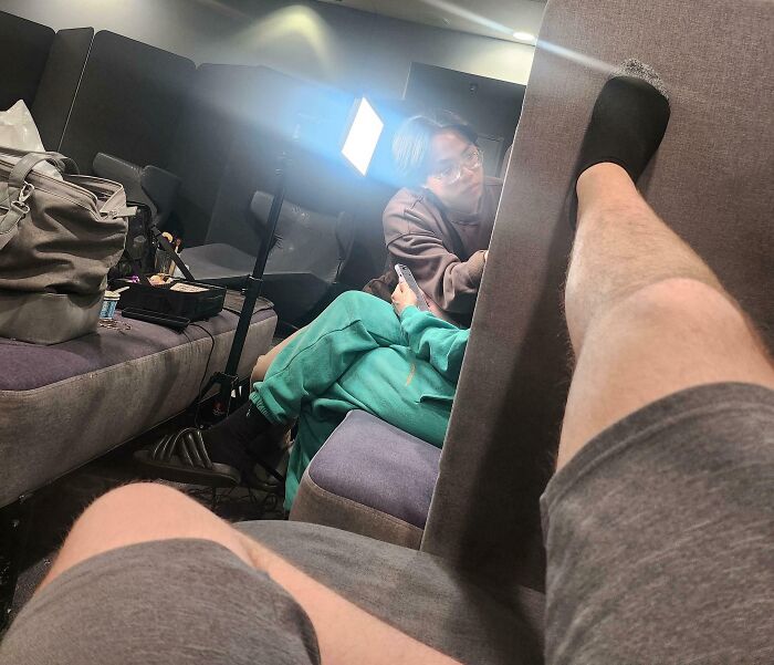 Passenger resting foot on seat divider invading another's space, annoyed traveler nearby, next-level jerks