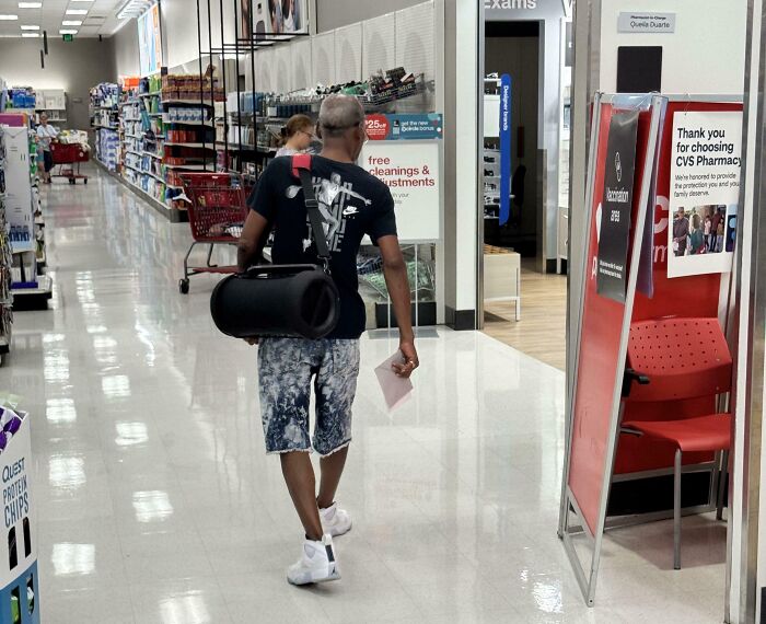 Man strolling through a retail aisle carrying a large rolled mat on his shoulder, next-level jerks