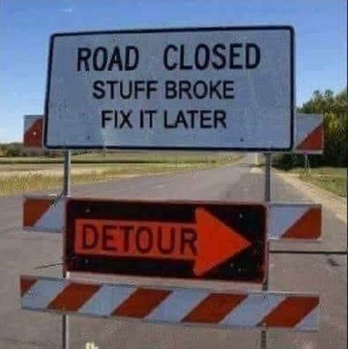 Road closed sign with funny stupid message stuff broke fix it later and an orange detour arrow on empty road.