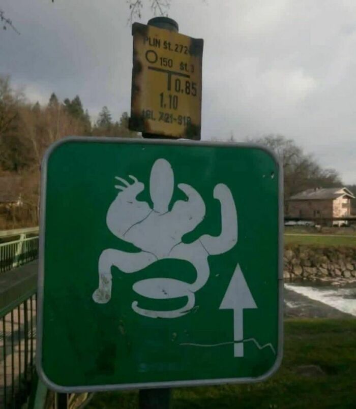 Funny stupid signs pic showing a distorted creature with multiple arms on a green directional sign outdoors.