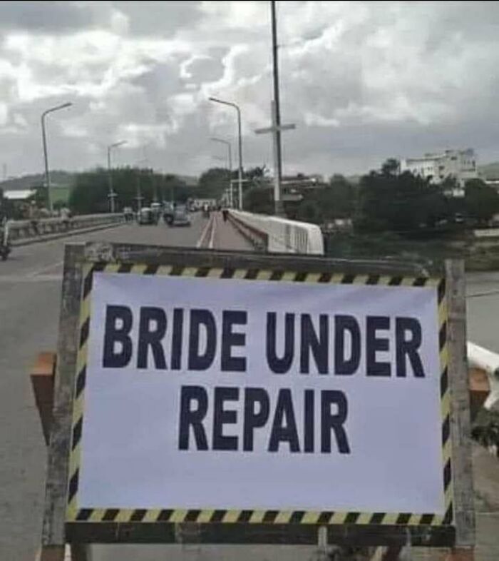 Sign on a roadside barrier with the funny stupid signs pics phrase bride under repair on a cloudy day.