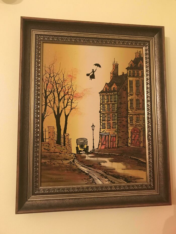 Framed thrifted painting of a vintage street scene with added funny silhouette of a person flying with an umbrella.