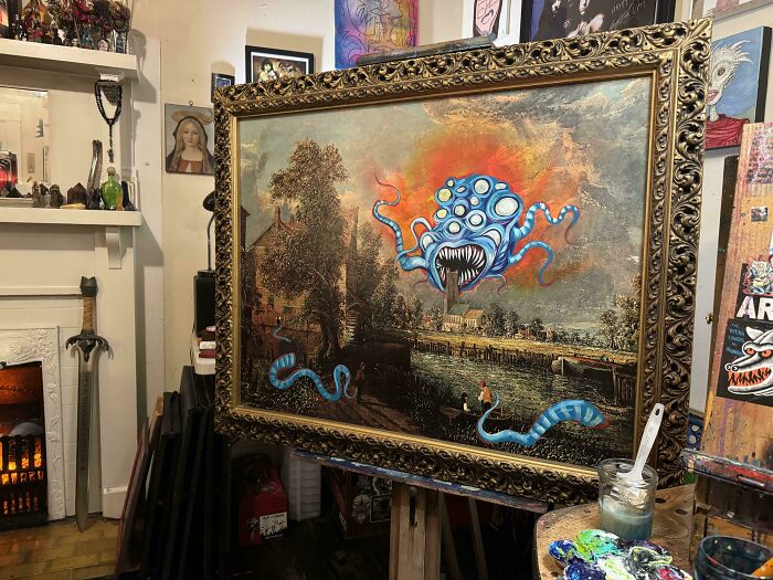 Thrifted painting personalized with a funny blue monster added to a traditional landscape in an artist’s studio.