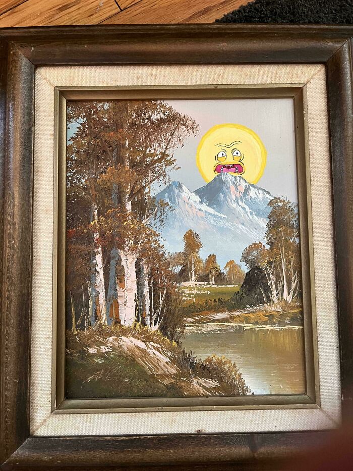 Thrifted landscape painting personalized with a funny cartoon sun face added over mountain peaks.