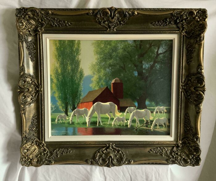 Thrifted painting of white horses grazing near a red barn, personalized with an unexpected humorous addition in an ornate frame.