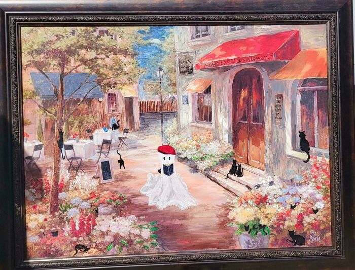 Person who personalized thrifted painting by adding a funny ghost with a red beret reading a book outdoors.