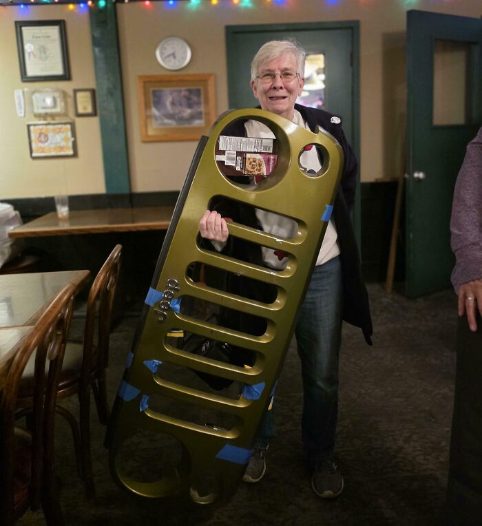 Person holding a large, bizarre object resembling a car grille received as a strange Christmas gift indoors.