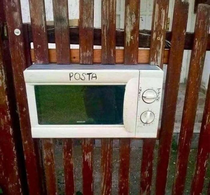 Old microwave repurposed as a mailbox attached to a wooden fence, illustrating funny Eastern Europe life hacks and memes.