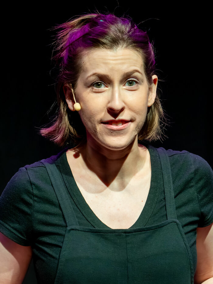 Eden Sher on stage wearing a black outfit and a microphone headset during a live performance.