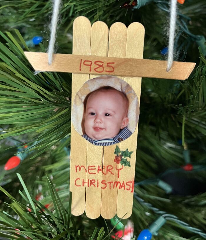 Baby photo Christmas ornament handmade from popsicle sticks hanging on tree, a sweet holiday moment that melts hearts.
