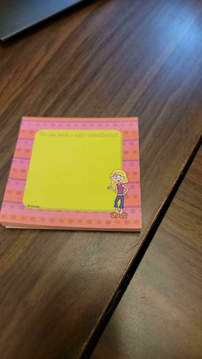 Sticky note with a 90s and 2000s nostalgia cartoon character on a wooden table, featuring a colorful border.