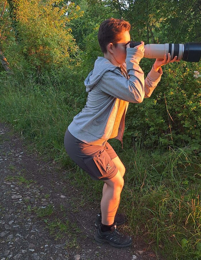 Person outdoors holding a camera with a large lens, capturing photos in nature, showing fun sibling moments.