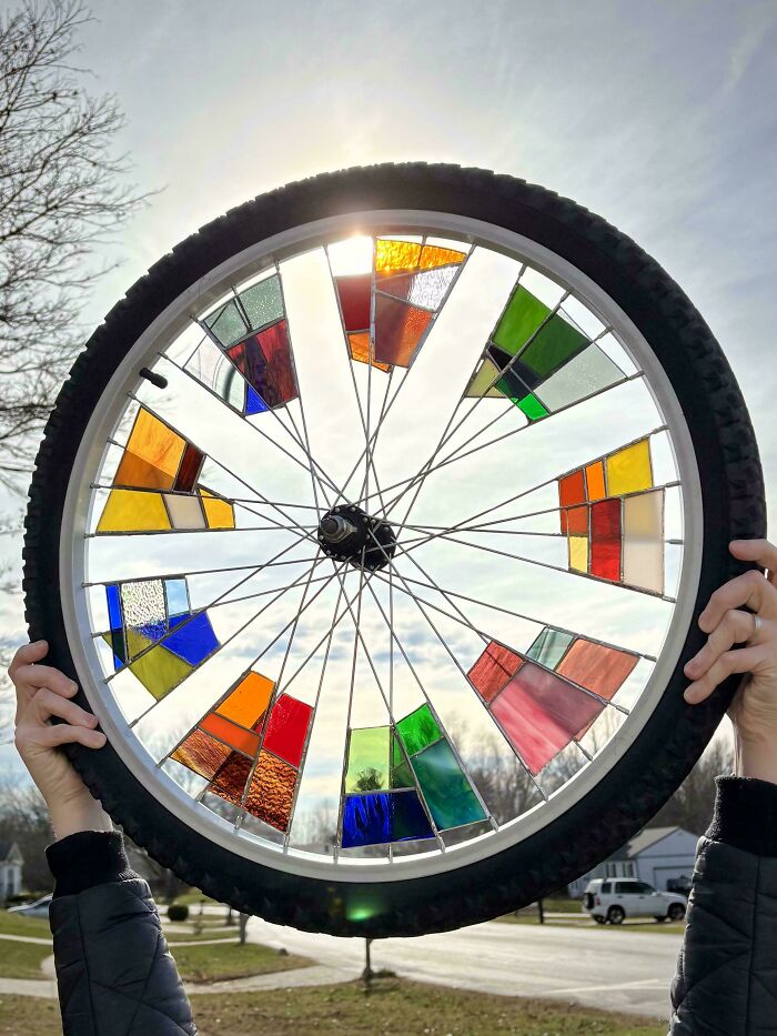 Bicycle wheel decorated with colorful stained glass panels held up outdoors on a bright day, holiday moments concept.