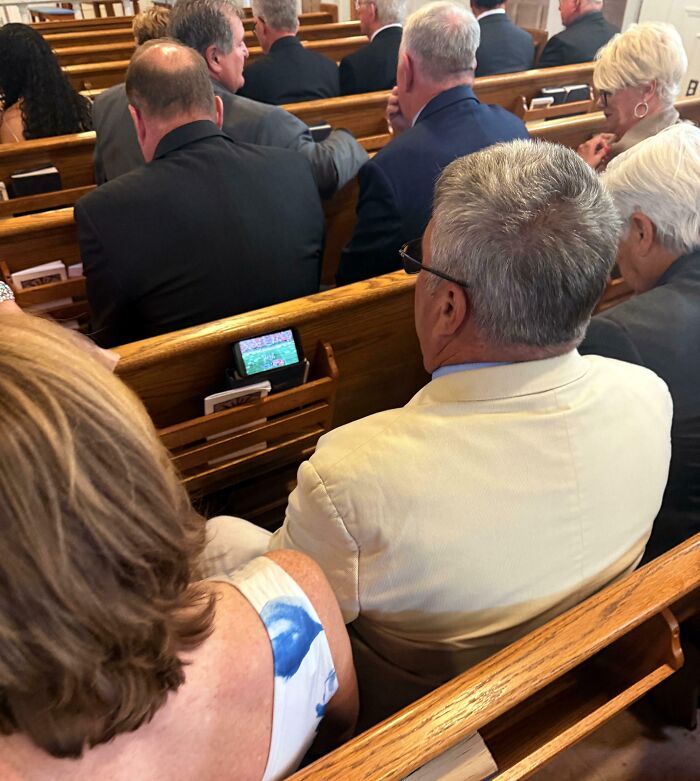 Funny Pictures: man in beige jacket watching football on phone mounted to church pew during service