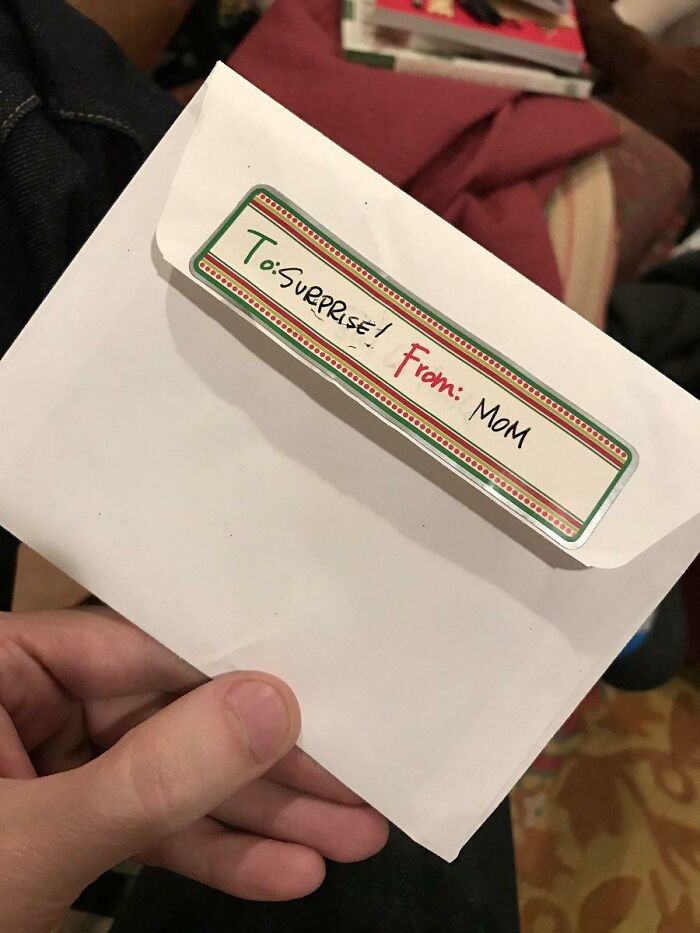 Hand holding a white envelope with a label reading To Surprise From Mom, example of bad Secret Santa gifts.