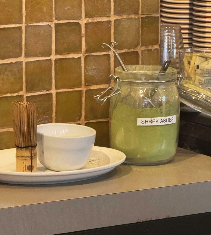 Funny Pictures 2025 jar labeled SHREK ASHES with green powder, matcha whisk and bowl on tiled counter