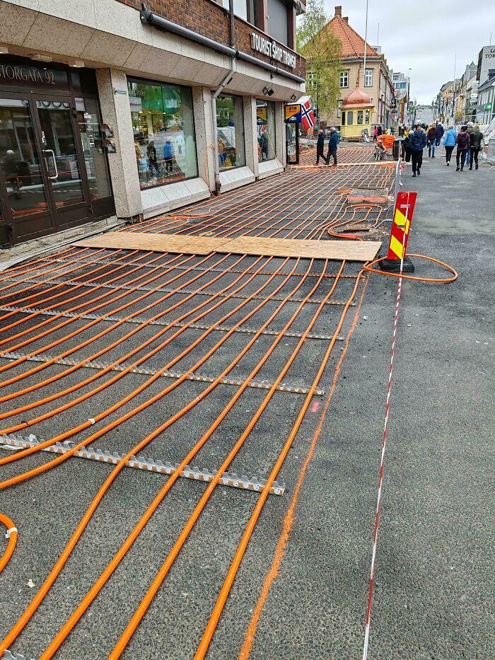 Heated sidewalk installation with orange heating cables laid out on a busy street, showcasing impressive country innovations.